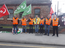 An RMT picket line with strikers in orange hi-vis vests with green and red RMT flags 