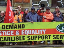 Striking RMT members with a union banner reading "WE DEMAND JUSTICE & EQUALITY FOR CARLISLE SUPPORT SERVICES WORKERS"