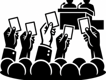 Silhouette-style icon of a public vote or assembly. Several raised hands hold voting cards in front of a crowd, while two speakers sit at a podium with microphones, suggesting a meeting, conference, or democratic decision-making process.
