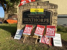 Photo shows a stone marker reading "Welcome to Hexthorpe: Home of the Flying Scotsman", adorned with RMT and Unite picket signs, flags, and placards