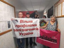 A group of people stand in a hallway holding union banners. The front banner, written in Ukrainian, reads 'Вільна профспілка залізничників України' (Free Trade Union of Railway Workers of Ukraine). A woman on the right holds a pink banner that says 'Solidaires Union Syndicale'. Behind them, other individuals hold additional union flags, partially visible in black and red.
