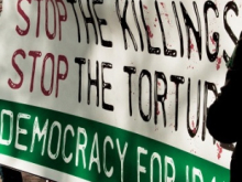 A large protest banner reading ‘Stop the Disappearances, Stop the Killings, Stop the Torture, Democracy for Iran,’ held by people partially visible at the edges of the image.