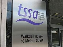 Metal sign outside the former TSSA headquarters reading "tssa – the union for people in transport and travel," with the address "Walkden House, 10 Melton Street." A glass entrance door is visible beside the sign.
