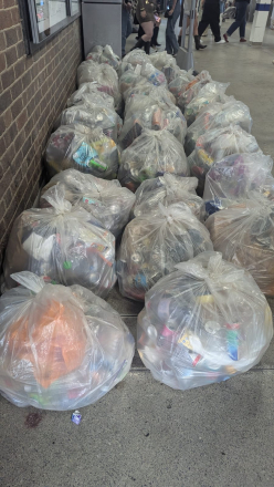 A large pile of clear plastic bags filled with rubbish stacked along the wall of a London Underground station concourse, with passengers walking in the background.