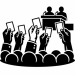 Silhouette-style icon of a public vote or assembly. Several raised hands hold voting cards in front of a crowd, while two speakers sit at a podium with microphones, suggesting a meeting, conference, or democratic decision-making process.