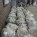 A large pile of clear plastic bags filled with rubbish stacked along the wall of a London Underground station concourse, with passengers walking in the background.